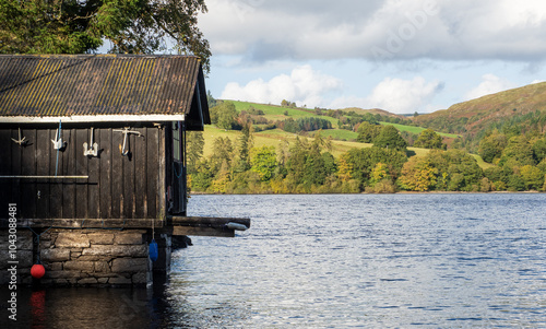 An old wooden boathouse on the lake with green landscape behind in the distance.