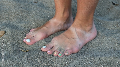 tanned bare female feet with light stripes from sandals on gray fine textured sand, close-up, harmony and relaxation of girl on beach barefoot