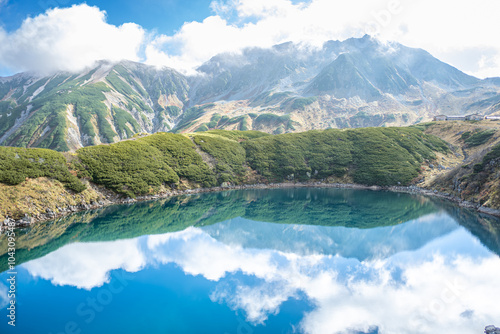 Murodo, Tateyama Kurobe Alpine Route, Japan, A serene landscape featuring a calm lake reflecting mountains and clouds under a bright blue sky photo