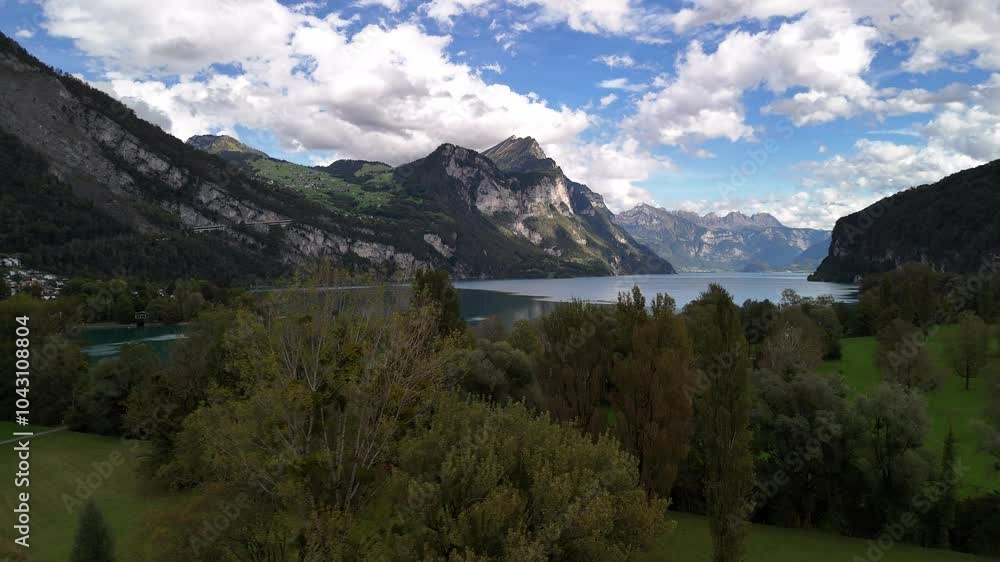 Daytime aerial view of Lake Walensee, Switzerland, where fluffy clouds and mountains reflect gracefully on the water, forming a serene and picturesque natural landscape.