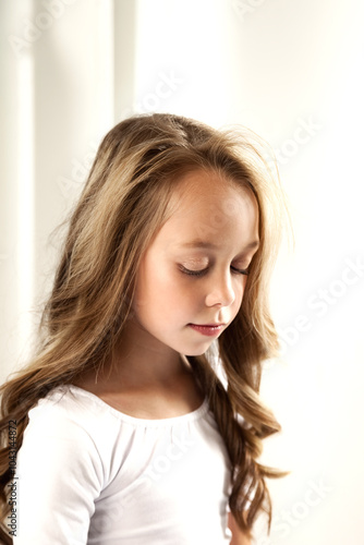 Portrait of perfect child girl 8 year old in white wear posing in white studio, closed eyes. Adorable little kid girl with hairstyle for advertising. Trendy youth fashion concept. Copy ad text space