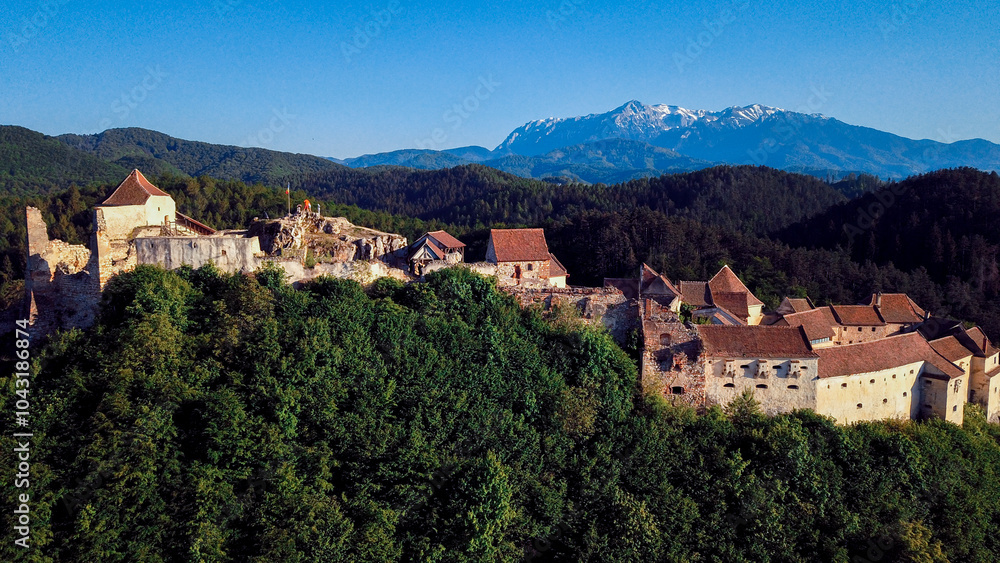 Obraz premium Rasnov Castle perched on a hilltop with snow capped mountains visible in the background