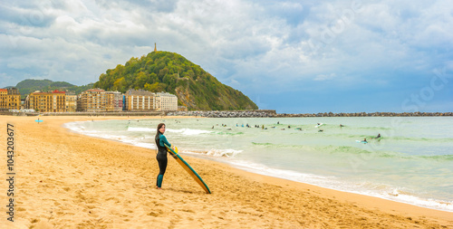 A surfer at Zurriola Beach with downtown San Sebastián and Monte Urgull in the background. Basque Country, Gipuzkoa, Spain.