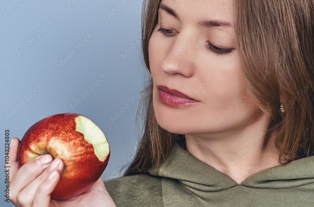 Close-up bitten red apple held by smiling woman. Concept of healthy food and diet. Gray background. Close-up bitten red apple held by smiling woman. Concept of healthy food and diet. Gray background.