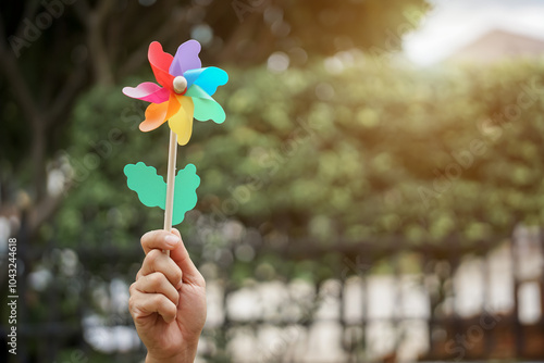 A woman joyfully holds a colorful pinwheel and a flower in her hands while standing in a vibrant garden under a blue sky on a breezy summer day
