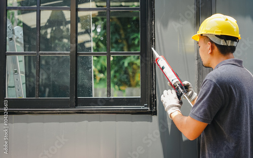 worker applying silicone sealant under window frame

