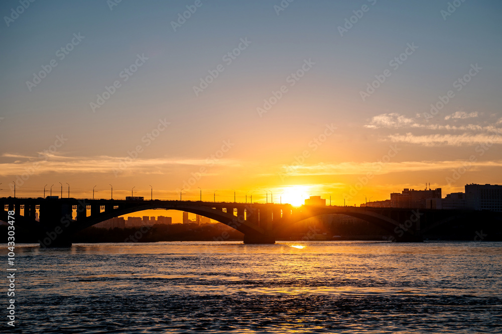 Fototapeta premium ducks swim in the Yenisei at sunset against the background of the communal bridge