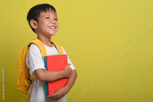 Asian boy happy holding books isolated on yellow background. Child with bright future. Back to school concept