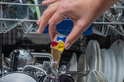 Woman putting detergen kapsul into open dishwasher photo