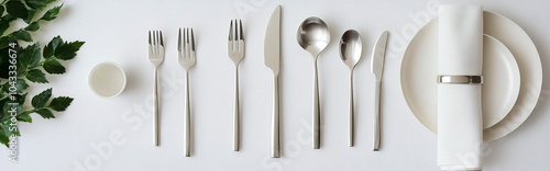 Stylish flat lay of cutlery and silverware on a white background, top view. Minimalist dining table setting with modern stainless steel spoons, knives, forks, a plate, and a napkin, with a green plant photo