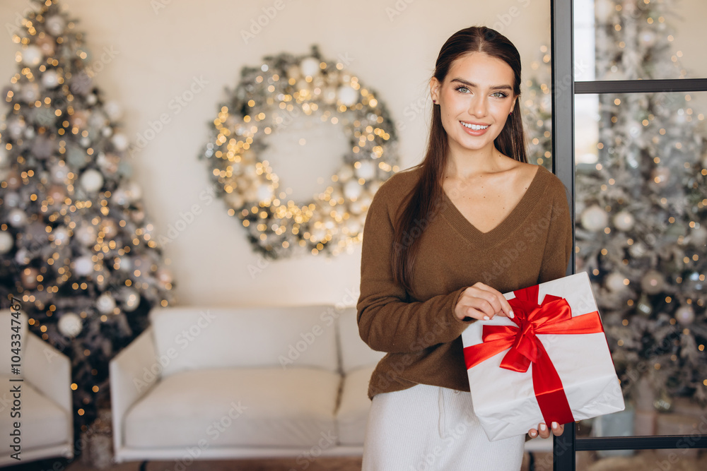 Smiling Woman Holding Christmas Gift in Festive Living Room Smiling Woman Holding Christmas Gift in Festive Living Room