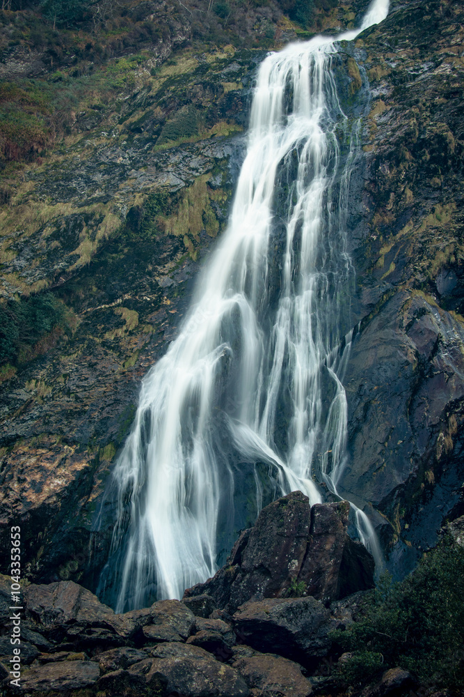 Obraz premium A waterfall is surrounded by rocks and trees in the mountains