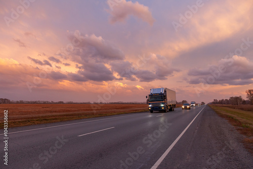 Road Leading Into A Sunset. View of Country road passing through fields during sunset. Asphalt road in rural landscape at sunset with dramatic clouds.