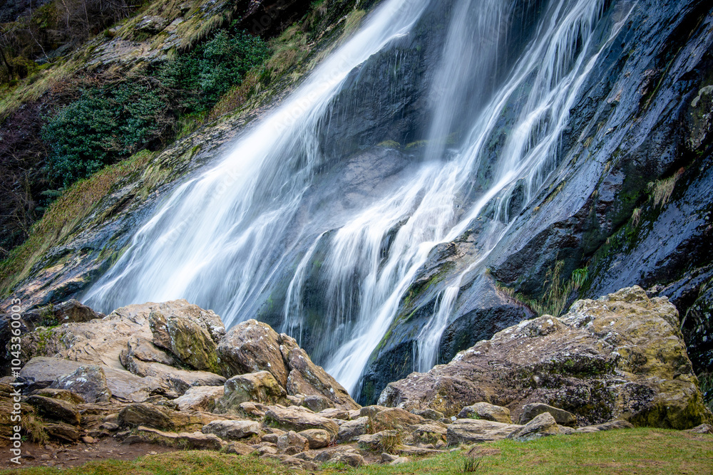 Obraz premium A waterfall surrounded by rocks and grass in a forest