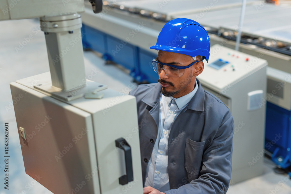 African American engineer with a blue helmet and safety goggles, operating a control panel, controlling and automating industrial processes. African American engineer with a blue helmet and safety goggles, operating a control panel, controlling and automating industrial processes.