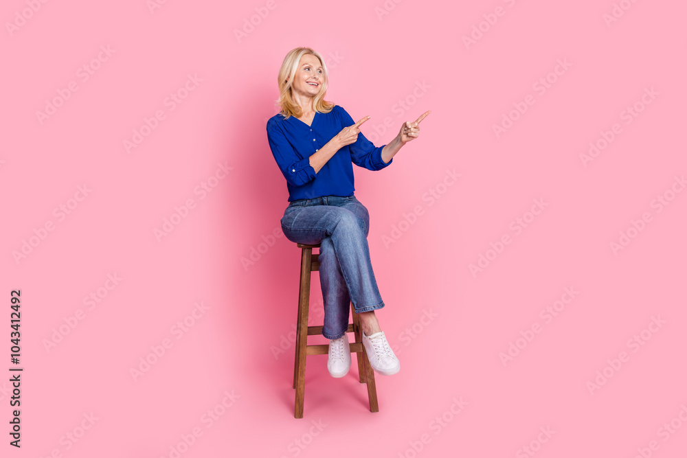 Fototapeta premium Full length photo of lovely pensioner lady sit chair look point empty space dressed stylish blue garment isolated on pink color background
