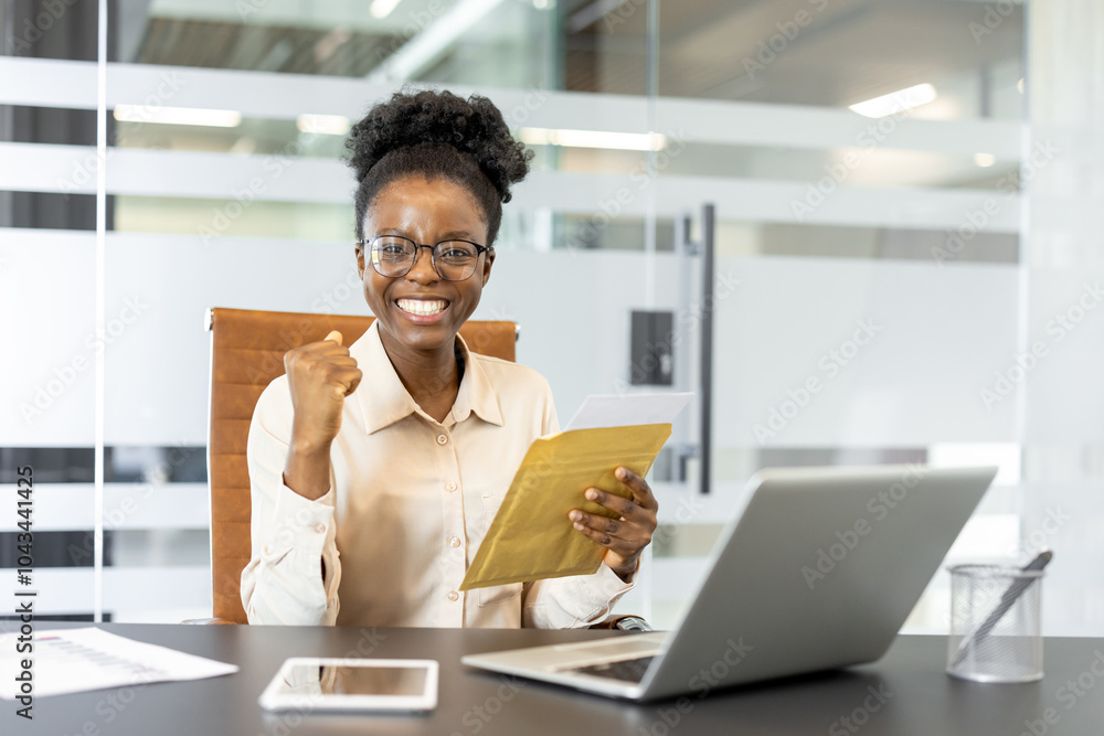 African American businesswoman celebrating success at office desk, holding documents with laptop and smartphone. Expresses excitement, achievement, and professional satisfaction in workplace setting. African American businesswoman celebrating success at office desk, holding documents with laptop and smartphone. Expresses excitement, achievement, and professional satisfaction in workplace setting.