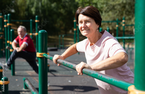 Elderly woman doing exercises on sports bars at outdoor sports ground