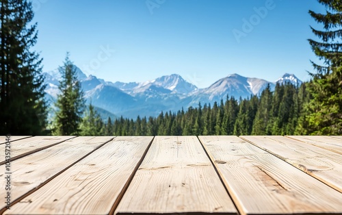 A scenic view of mountains surrounded by lush forests, with a wooden deck in the foreground, under a clear blue sky.