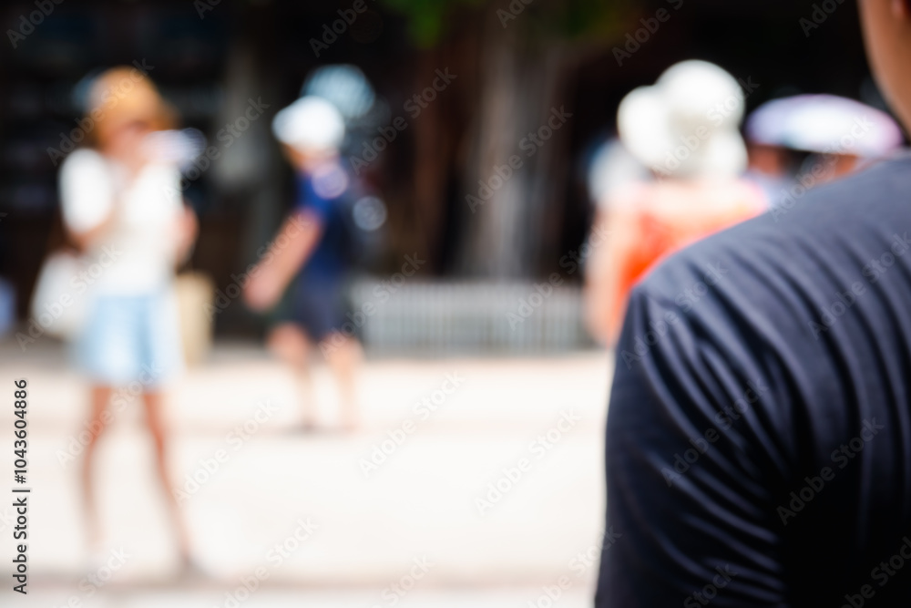 Obraz premium A blurry photo of a man and a woman in a park. The man is wearing a black shirt and the woman is wearing a white shirt. There are several other people in the background, some of them wearing hats