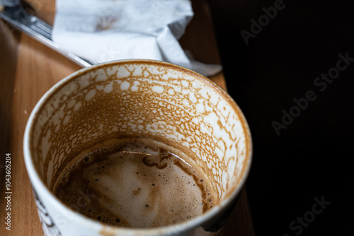 A coffee cup with a brown rim and a white interior. The cup is half full and has a few coffee stains on it photo