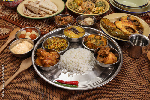 Bengali style thali spread verity cuisine hilsa fish vegetable beef mutton egg curry fry vorta mashed chicken liver sweet yogurt side dish served on rustic metal tin stainless steel plate small bowls photo