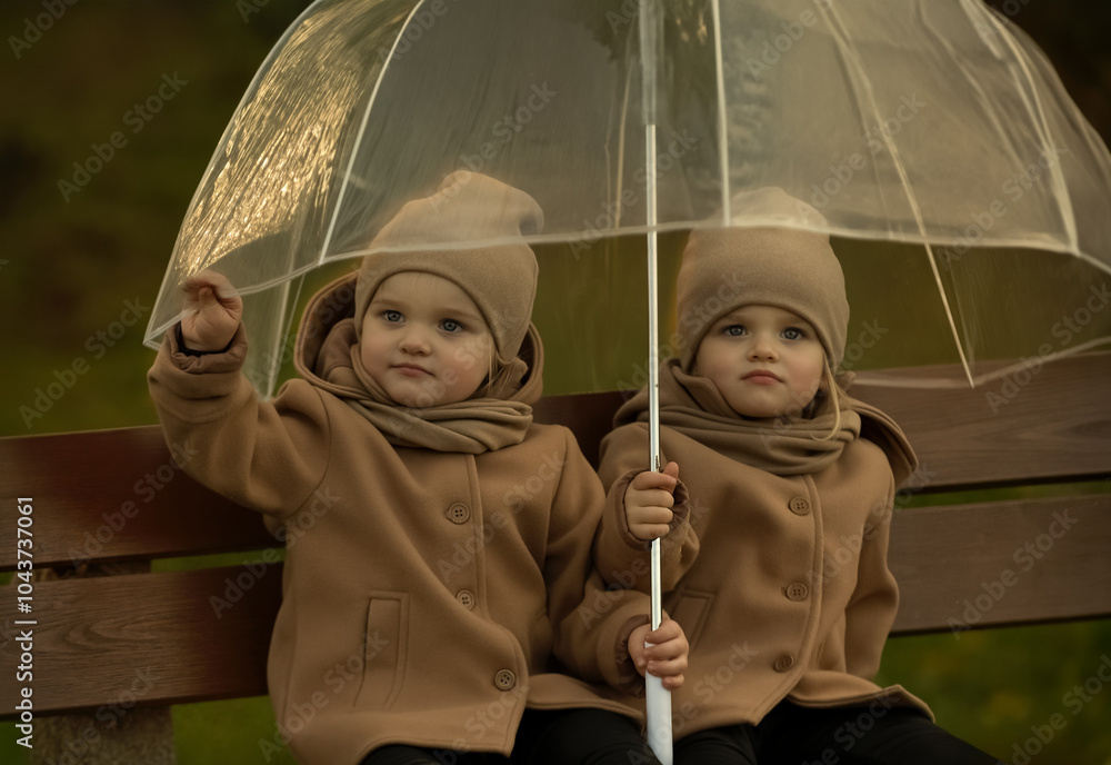 Artistic photograph of twin girls hugging under an umbrella in a park ...