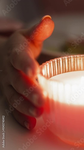 Woman hands turn burning candle in stylish glass holder sitting at table during festive dinner in semidark room extreme closeup slow motion photo