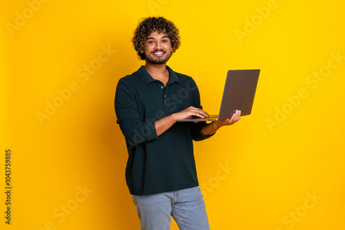 Young man smiling confidently while using laptop against vibrant yellow background, representing modern technology and creativity