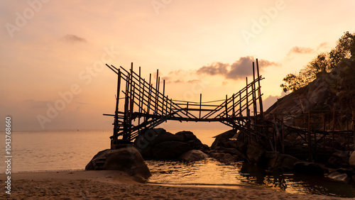 A wooden bridge spans a serene water body at sunset
