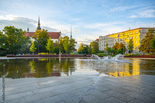 The fountain in Moravian Square showcases shimmering water reflections during a serene evening, with nearby buildings and trees enhancing the picturesque landscape of Brno.