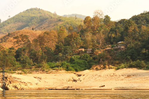 View from the slow boat from Thailand to Laos onto the shore of the Mekong River with a small village, settlement with bamboo huts, cabins, Laos photo