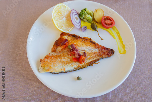 Obraz na płótnie Grilled sea bass in a white porcelain plate. Garnish: lemon, onion, tomato, capers, broccoli, potatoes, carrots. w salonie