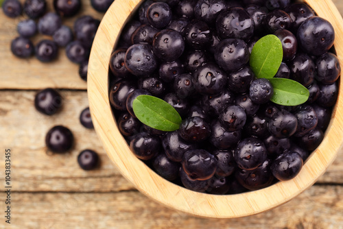 Ripe acai berries and leaves in bowl on wooden table, top view photo