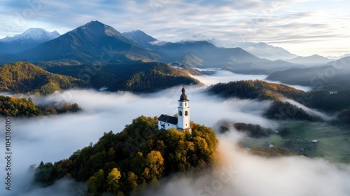 A picturesque church sits atop a hill enveloped by morning fog, surrounded by the breathtaking view of distant mountain ranges under a clear sky. photo