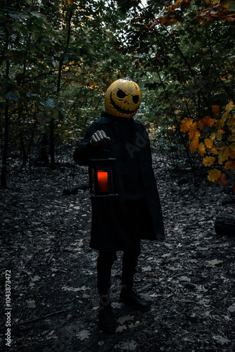The man Pumpkinhead Jack, stands in the woods in a cloak with a lantern and a red candle.