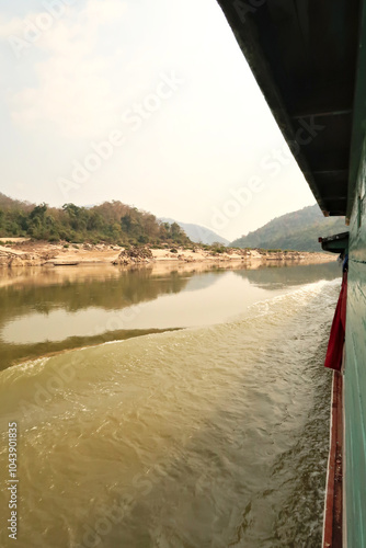 View from the slow boat from Thailand to Laos onto the Mekong River, the landscape is reflecting on the smooth surface of the water, Laos