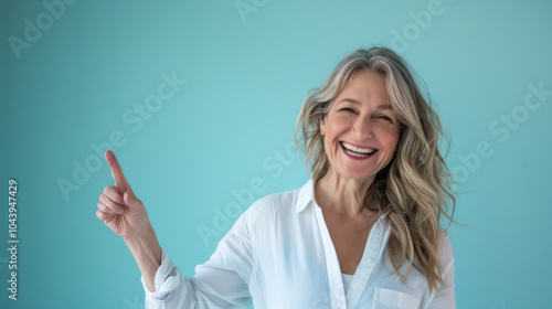 Smiling woman with long wavy hair points to the right against a light blue background in a casual setting