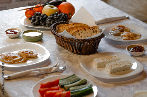 A cozy breakfast spread featuring a mix of fresh fruits, sliced vegetables, bread, cheese, and pancakes. The table is set with a rustic wicker basket for bread, creating a warm atmosphere 