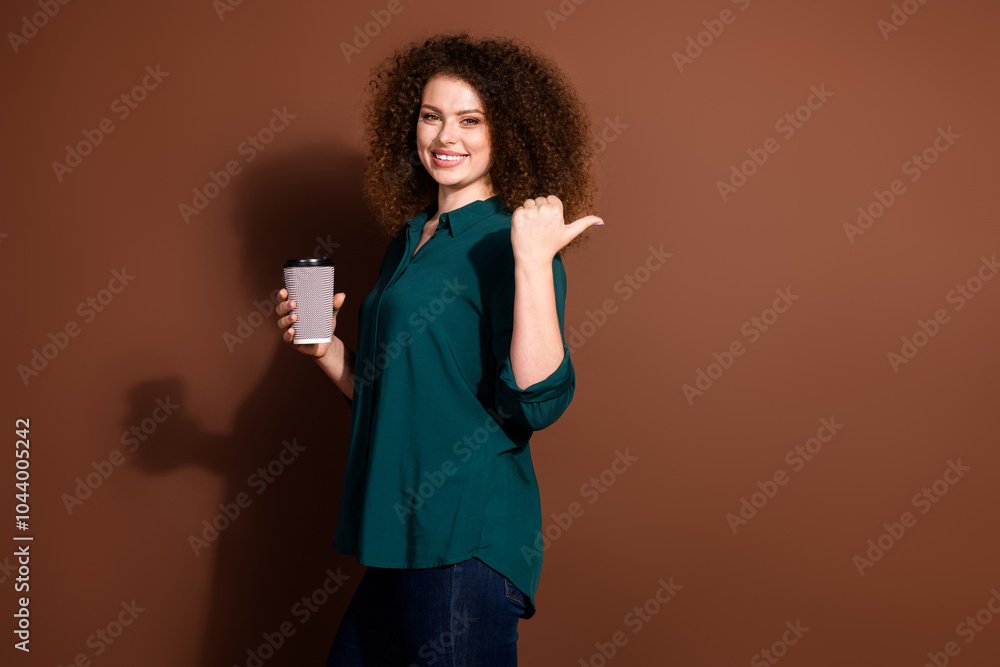 Photo of charming positive woman wear green shirt drinking coffee showing thumb empty space isolated brown color background Photo of charming positive woman wear green shirt drinking coffee showing thumb empty space isolated brown color background