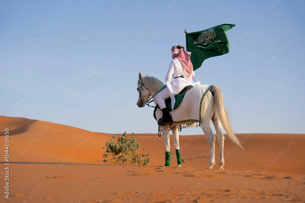 Man riding on a horse in the desert holding the Saudi flag