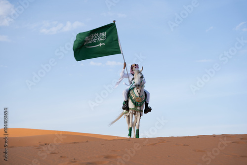 Man riding on a horse in the desert holding the Saudi flag
