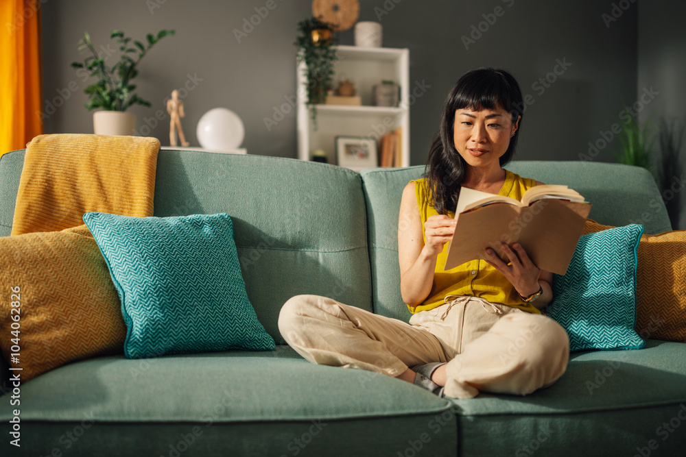 Obraz premium Relaxed asian woman reading a book on a stylish couch