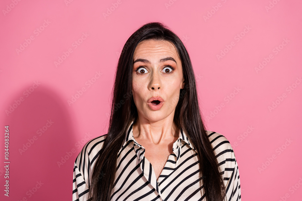 Fototapeta premium Surprised young woman in striped shirt against pink background showing shocked expression