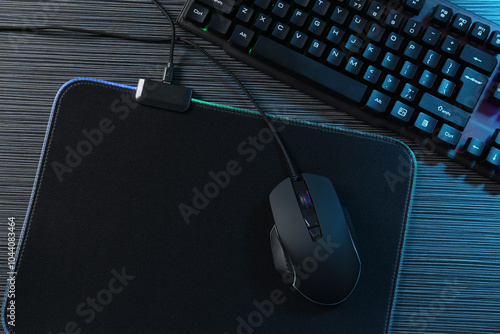 Computer mouse, mousepad and keyboard on dark wooden table in neon lights, flat lay