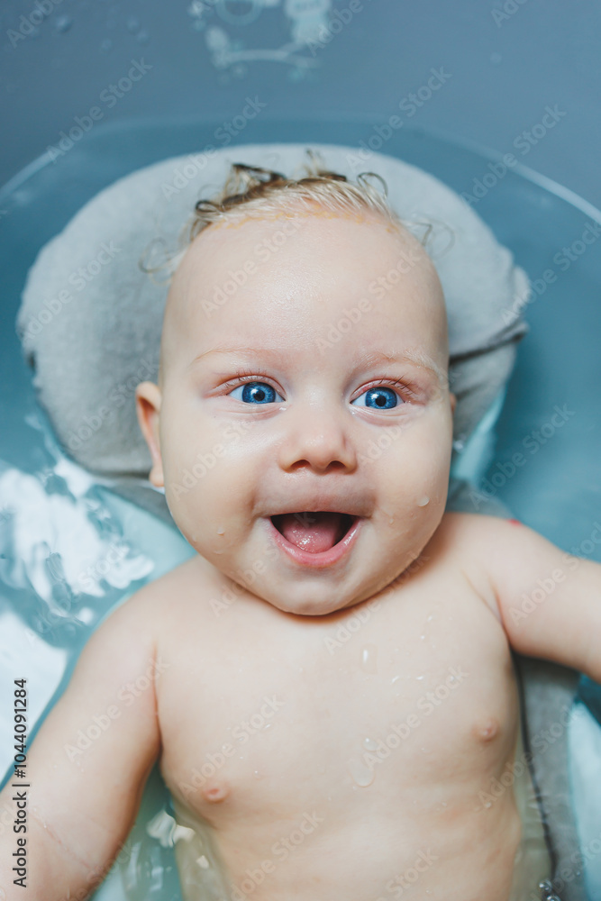 A baby boy is playing and smiling while sitting in a white bathtub with water. Bathing a baby. A baby boy is playing and smiling while sitting in a white bathtub with water. Bathing a baby.