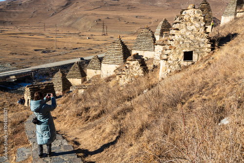 North Ossetia, Caucasus, Russia - 7 January 2021: A woman taking photos of The City of the dead, the Village of Dargavs of North Ossetia, Caucasus, Russia photo