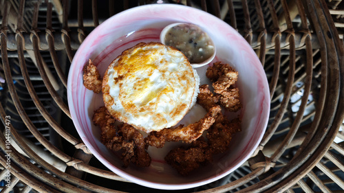 Golden fried egg served with crispy chicken bites and creamy mushroom sauce in a vibrant ceramic bowl, styled on a rustic rattan table, capturing a cozy cafe breakfast ambiance.