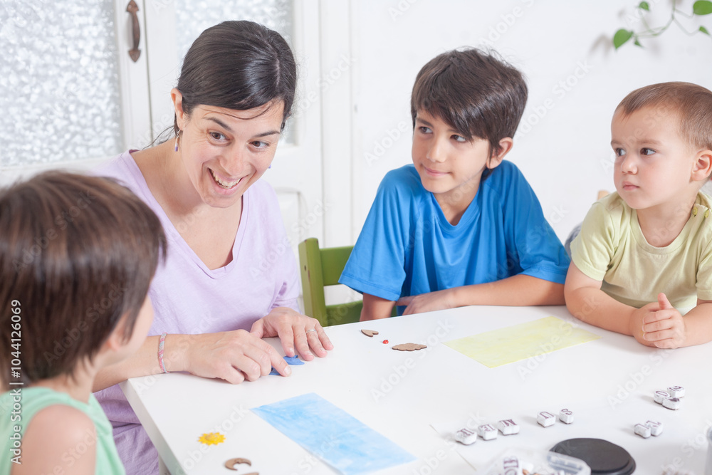 A woman sits at the table with her three children explaining a craft to them. A woman sits at the table with her three children explaining a craft to them.