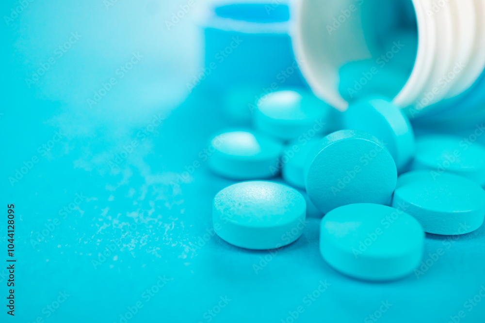 Overturned white plastic bottle with blue pills spilling out of it. Blue pills or vitamin supplements on blue background with copy space. Overturned white plastic bottle with blue pills spilling out of it. Blue pills or vitamin supplements on blue background with copy space.